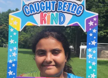 girl posing with a colorful sign that says Caught Being Kind