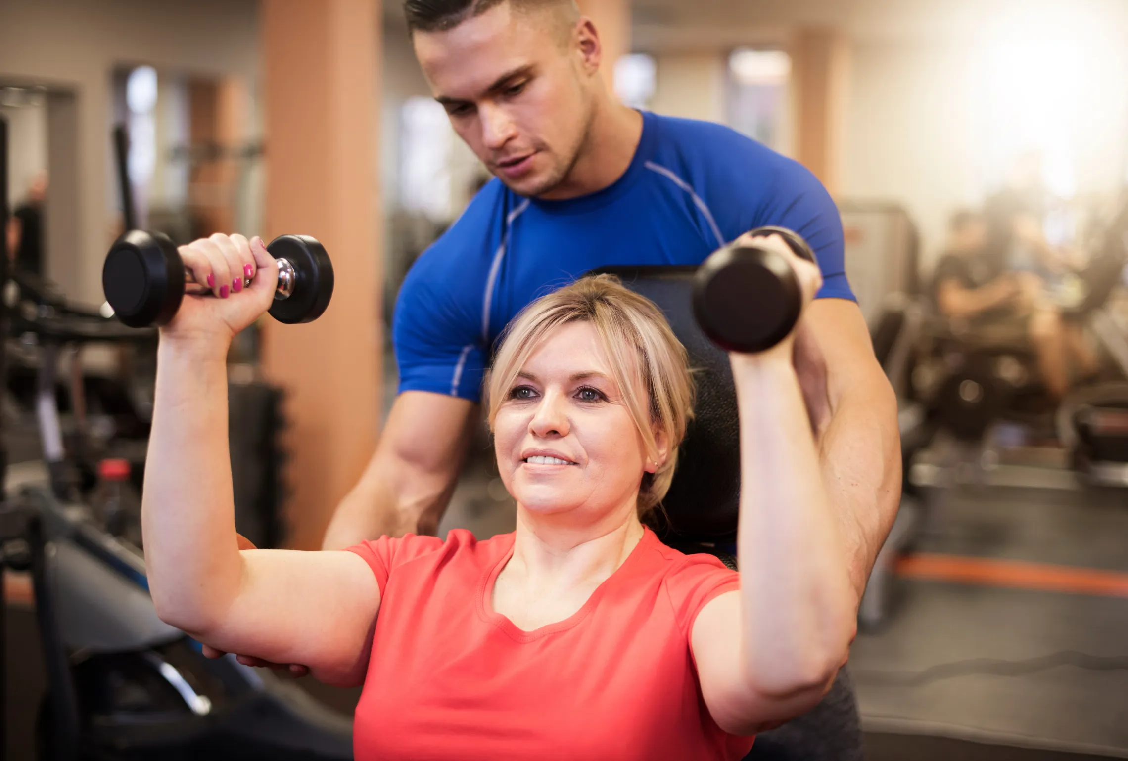 woman lifting weights with help from a personal trainer