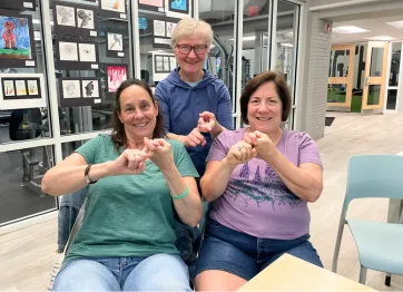 three women signing "friend" in ASL